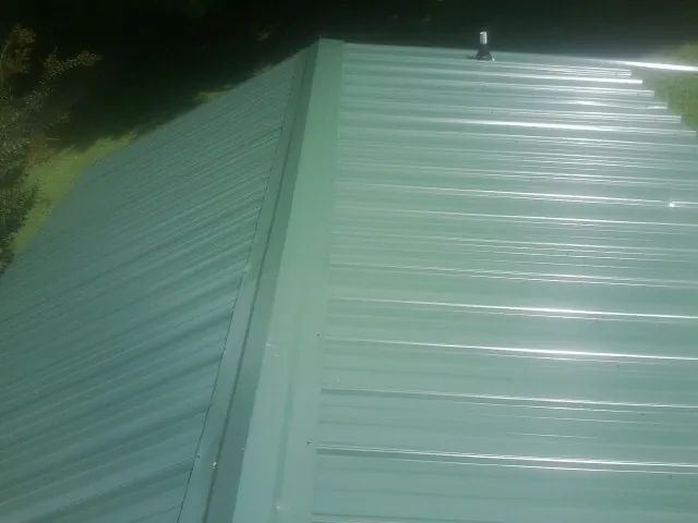 New green metal panels meeting at the ridge of a roof — Flat Roof Repair work by our crew in Erin