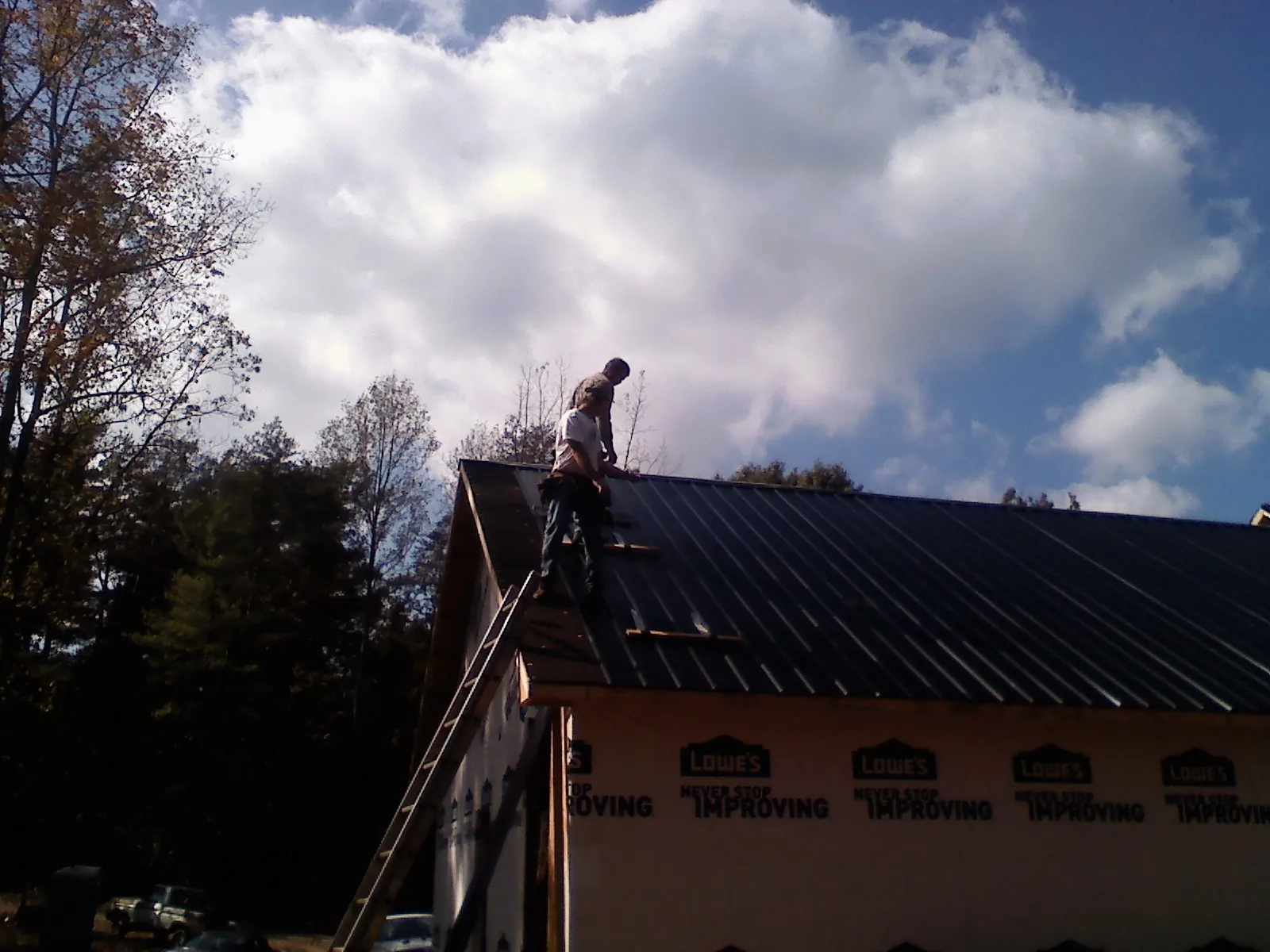 Roofer fastening dark metal panels high against a cloudy sky, from a Roof Inspection job in Erin