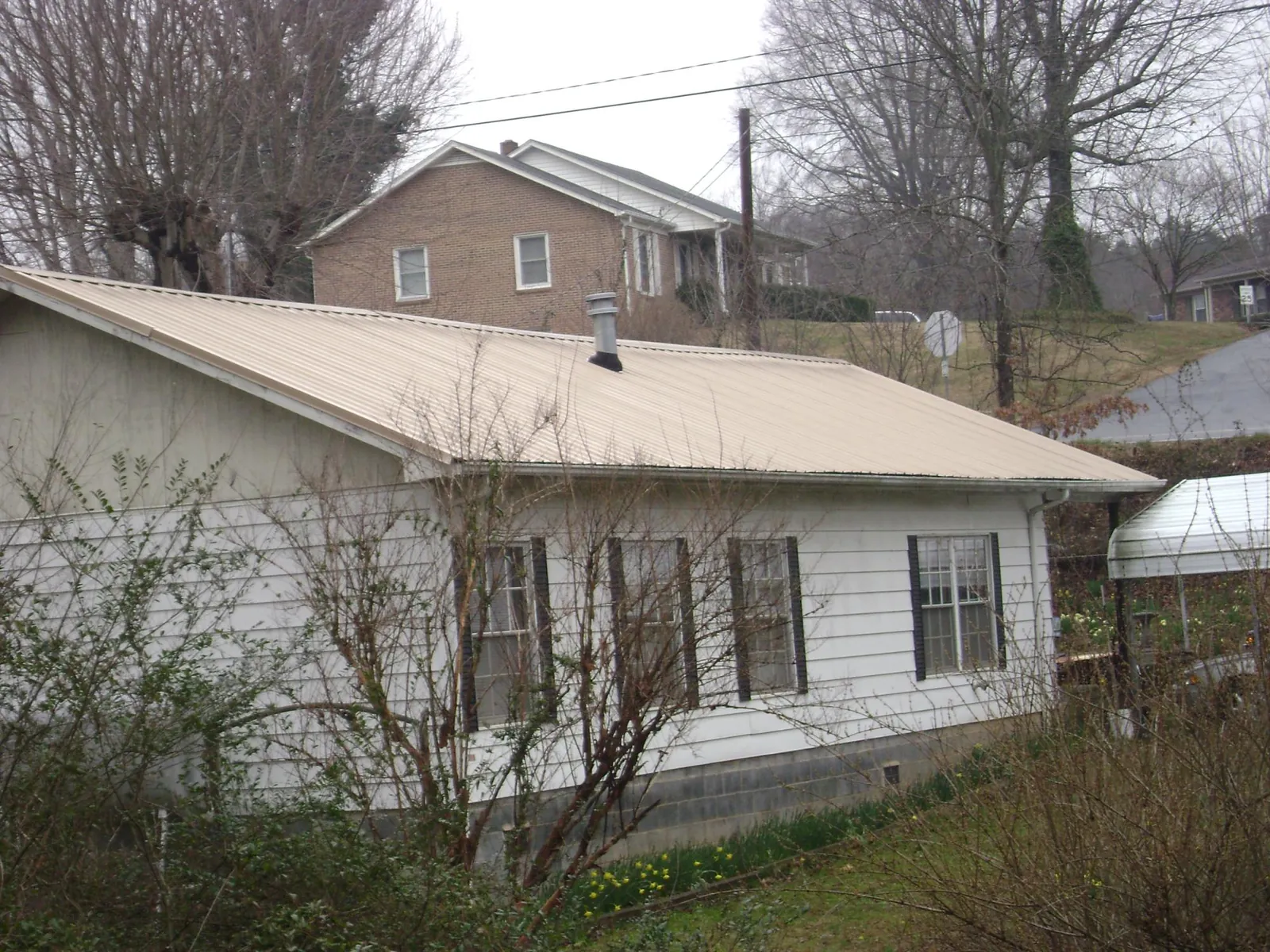 Tan metal roof on a white sided house set into a hillside — Commercial Roofing by Roofing Brothers in Erin